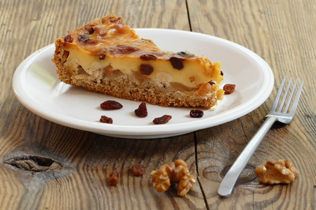plate with a piece of cake on an old rustic wooden board, some raisins, walnuts and a cake forkの写真素材