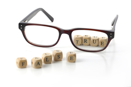 message "false" in blurry letters and "true" in sharp letters behind glasses, written in wooden blocks, isolated on white background symbol, conceptの写真素材