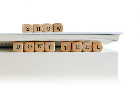 message - show do not tell - for creative writing, spelled with wooden letter blocks on the top and between pages of a big white book or skript stack, isolated on white, copy spaceの写真素材