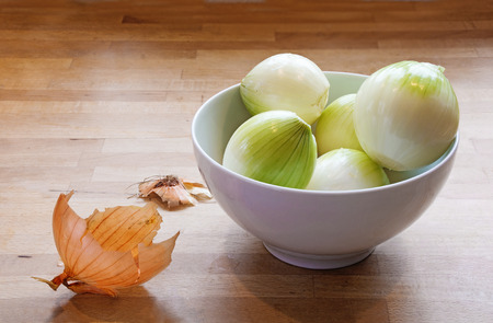 peeled onions in a bowl and onion peel on a wooden worktop, copy space in the backgroundの写真素材