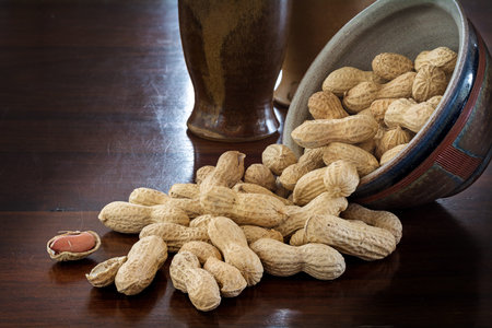 peanuts in shells and rustic ceramic tableware on a dark brown table, copy space in the background