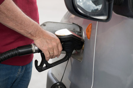 hand of a man holding gasoline pump into the tank of a car