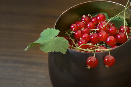 red currants and leaves in a metal  bowl against brown background with copy spaceの写真素材
