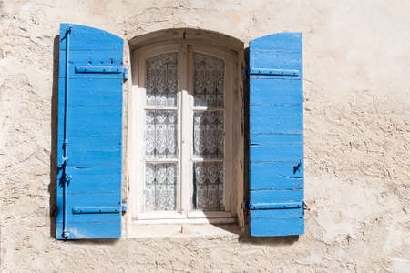 old window with blue shutters and lace curtain in a rough-plastered wall, copy spaceの写真素材