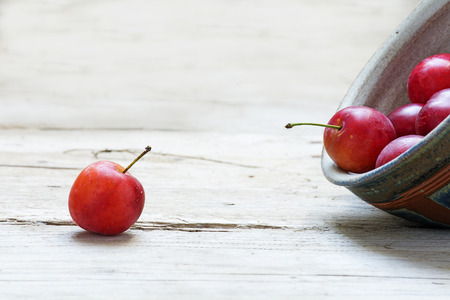 Still life with a single red wild plum and towards more in a tilted bowl on faded wood, copy spaceの写真素材