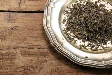 loose black tea on a silver plate on rustic brown wood, view from above, corner background with copy spaceの写真素材