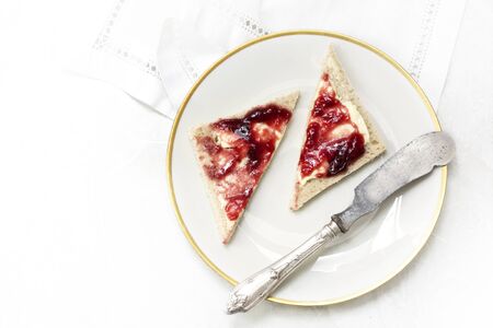 sandwich with red jam on a white plate with a gold rim and an old silver knife, view from above with copy spacethe background fades to white,の写真素材