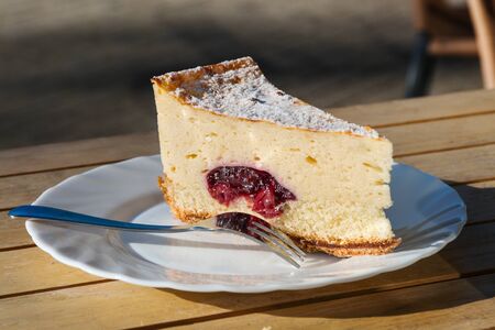Slice of cheesecake with cherry filling on a white plate on a wooden tableの写真素材