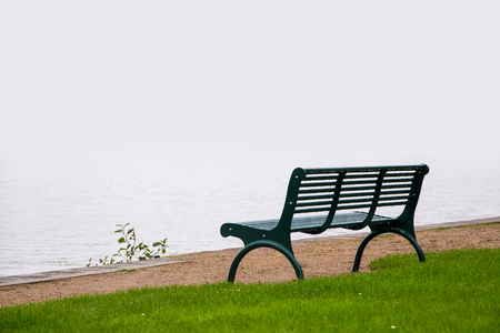 empty park bench, wet from the rain on the shore of a misty lake, concept for evening of life and farewell, copy spaceの写真素材