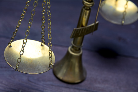 Part of scale or scales of brass on a dark wood showing law justice or legal concept, selected focus and narrow depth of fieldの写真素材