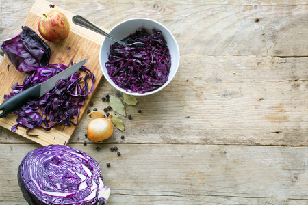preparing red cabbage for a festive dinner with apple, onion, bay leaves and juniper berries on a rustic wooden table, view from above, copy spaceの写真素材