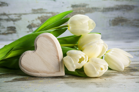 white tulips and a heart of wood on a vintage gray wooden background, love concept, closeup with selected focus and narrow depth of fieldの写真素材