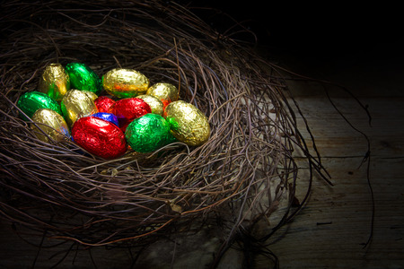 natural easter nest with colorful wrapped chocolate eggs on a rustic wooden table, copy space in the dark background, closeup with selected focus and narrow depth of fieldの写真素材