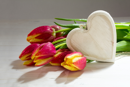 Bouquet of fresh tulips in red yellow and a wooden heart, love decoration for Easter, Valentine's Day or Mother's Day, selected focus and copy spaceの写真素材