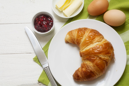Sunday breakfast with croissant, jam and egg, green napkin on white painted wooden table, copy spaceの写真素材