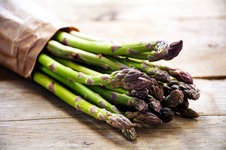 green asparagus bunch in brown paper on a rustic wooden board, closeup with selected focus and narrow depth of fieldの写真素材