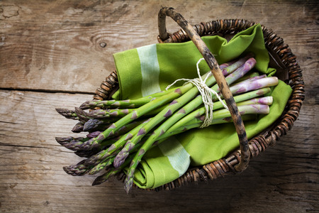 fresh green asparagus in a basket on a rustic wooden table, view from above, selected focusの写真素材