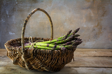 fresh green asparagus in a basket on a rustic wooden table in front of a vintage wall with copy space in the background, selected focusの写真素材