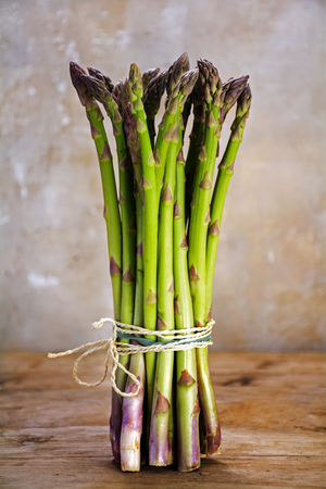 bunch of fresh green asparagus standing on a rustic wooden table, selected focus and narrow depth of fieldの写真素材