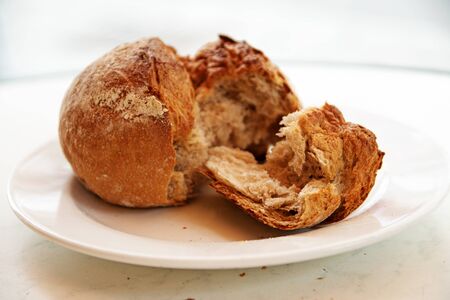 crusty wholegrain bun or bread roll from rye flour for breakfast and dinner, broken on a white plate, selected focus and very narrow depth of fieldの写真素材