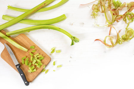 rhubarb stalks and spirals from the peel, sliced pieces and a kitchen knife on a cutting board, bright painted wooden background fades to white, view from above, copy spaceの写真素材