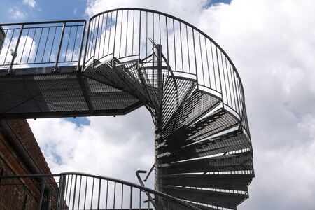 modern exterior spiral staircase from metal at an old building against a cloudy skyの写真素材