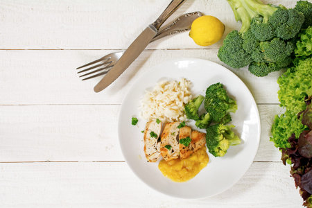 fried chicken breast fillet with a fruity sauce, broccoli and rice and the ingredients on a white painted wooden background, top view from above, generous copy spaceの写真素材
