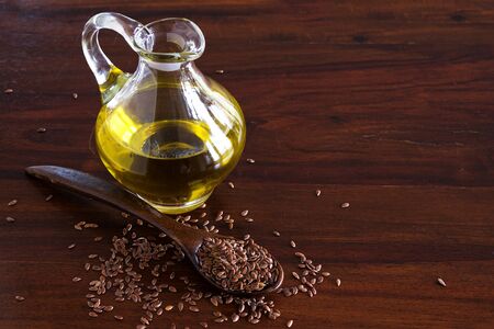 flax seeds on a spoon and linseed oil in a glass jug on a dark wooden table, copy spaceの写真素材