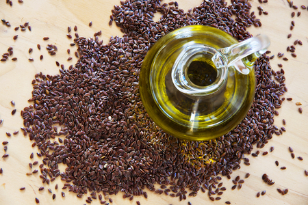 Brown flax seeds and linseed oil in a glass jug on a wooden kitchen board, top view from aboveの写真素材