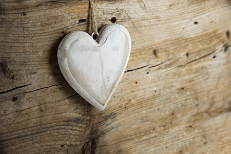 White heart shape made of wood hanging on a rustic wooden wall with copy space, concept for love, valentines and mothers day, selective focus, very narrow depth of fieldの写真素材
