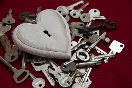 White wooden heart shape with a keyhole on a lot of keys, but no one fits and can unlock it, concept of the one true love, valentine's or mother's day, red fabric backgroundの写真素材