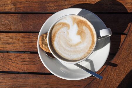 Coffee cup with cappuccino and milk foam on a wooden table outdoors in the summer, view from above, copy space, selected focusの写真素材