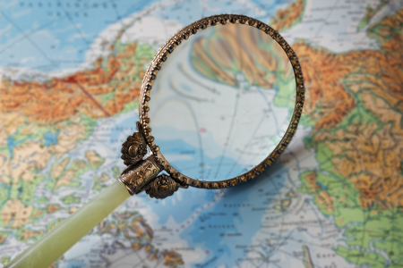 vintage magnifying glass on a blurred map, symbol for travel and wanderlust, selected focusの写真素材