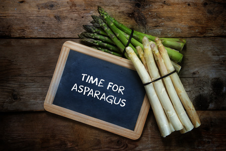 Green and white asparagus and a  blackboard with text time for asparagus,  on a rustic wooden background, top view from above, copy space, selective focusの写真素材