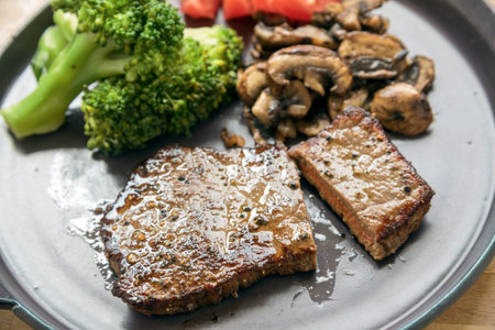 beef steak with vegetables like broccoli, champignons and tomatoes, low carb diet dinner on a gray plate, selected focus, narrow depth of fieldの写真素材