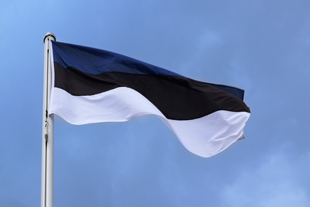 Flag of Estonia with stripes in blue, black and white, national symbol or sign of the country, fluttering in the wind against the blue sky with clouds on a sunny dayの写真素材