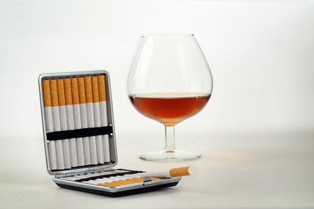 Tobacco and alcohol, cigarette case with filter cigarettes and a glass with cognac or brandy on a light gray background with copy space, health concept,  selected focus, narrow depth of fieldの写真素材