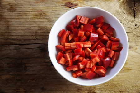 sliced red peppers in a white bowl on a rustic wooden background with copy space, preparing vegetables for cooking, top view from above, selected focusの写真素材