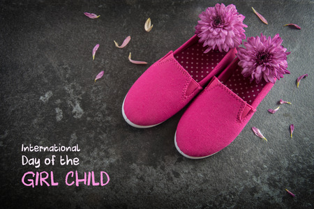 pink kid shoes and flowers on a dark slate background, text  International Day of the Girl Child,  concept date 11 October, copy space, selected focusの写真素材