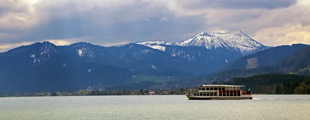 excursion boat in the lake tegernsee with blue and snow covered mountains in the background, panoramic view on the famous tourist resort in the Bavarian Alps, Bavaria, Germany, Europeの写真素材