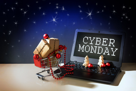 cyber monday online shopping, christmas baubles and gift boxes in a shopping cart driving out of a laptop with text, dark stars sky background, copy space, selected focusの写真素材