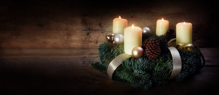 Advent wreath with four white burning candles and christmas decoration on rustic dark wood, panorama format with copy space, selected focus, narrow depth of fieldの写真素材