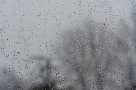 rain drops at a window, blurry bare trees  in the background, bad weather concept, copy spaceの写真素材