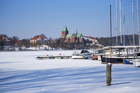Cathedral or Dom of Ratzeburg at the frozen lake in northern Germany at a sunny winter day, view from the sailing port, copy spaceの写真素材