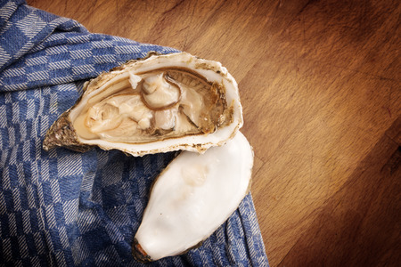 open fresh oyster on a blue kitchen towel on a rustic wooden table, copy space, selected focus, narrow depth of fieldの写真素材