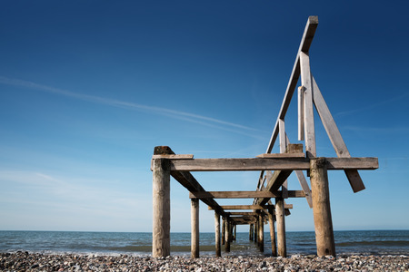 Broken wooden pier or jetty leads into the sea against a blue sky, perspective from below, copy spaceの写真素材