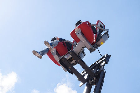 child sits on carousel seats mounted on a forklift and drives upwards into the blue sky, carnival fun on the funfair, copy spaceの写真素材