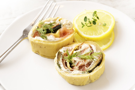 appetizer from smoked salmon, zucchini and cream cheese rolled in thin pancake with dill garnish on a white plate, selected focus, narrow depth of fieldの写真素材