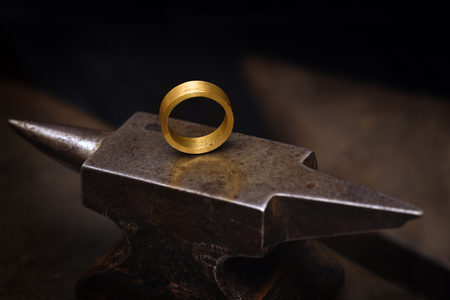 ring from gold on a goldsmith anvil in the jewelry manufactory, still life with copy space in the dark background, selected focus, narrow depth of fieldの写真素材