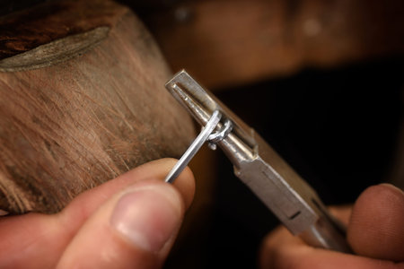 Goldsmith hands wrap silver wire with pliers in a spiral for small chain rings, macro shot with copy...
